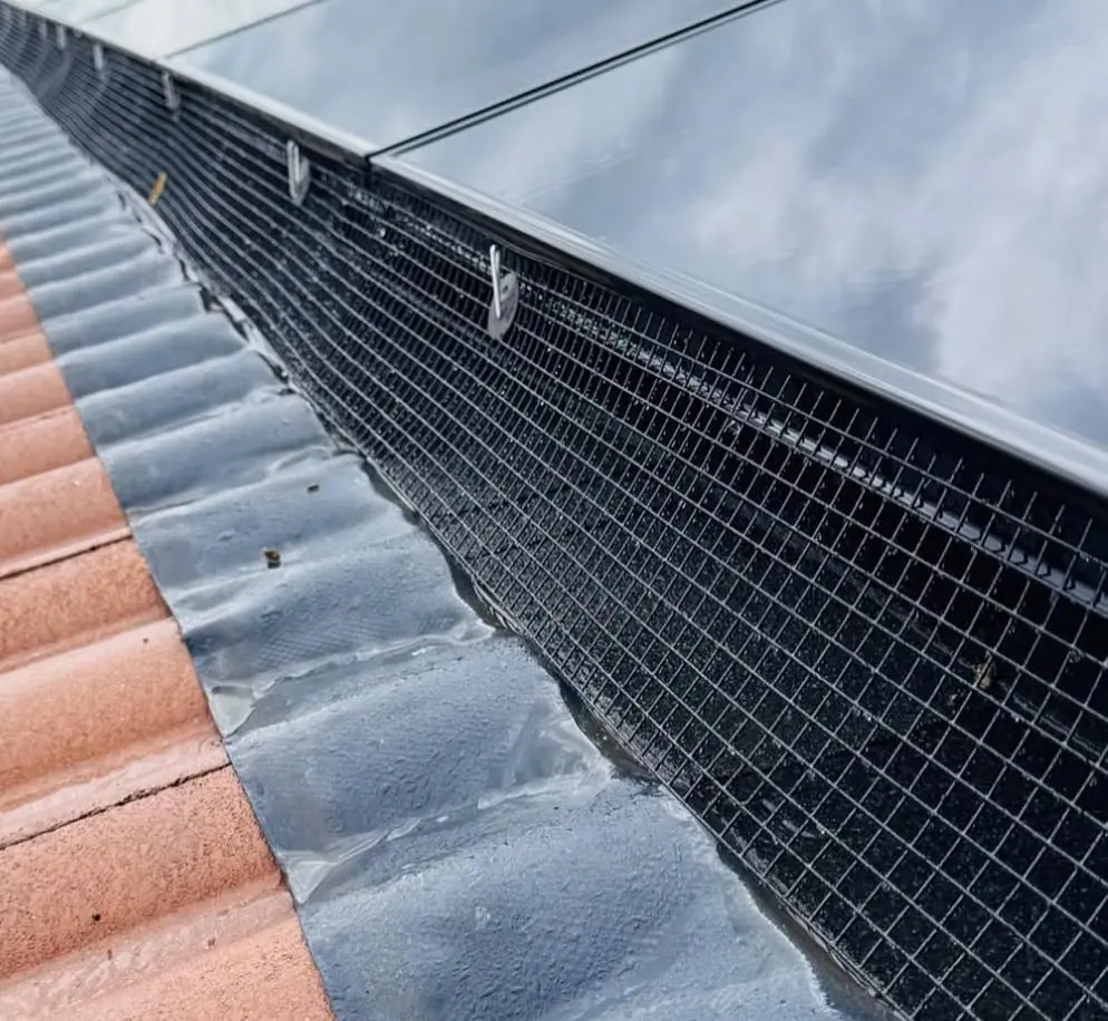 Black exclusion mesh following roof tile contours beneath solar panels