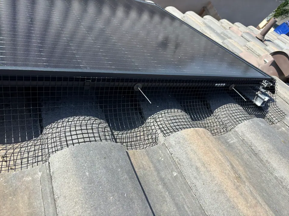 Bird guard mesh following curved roof tiles beneath a solar panel edge