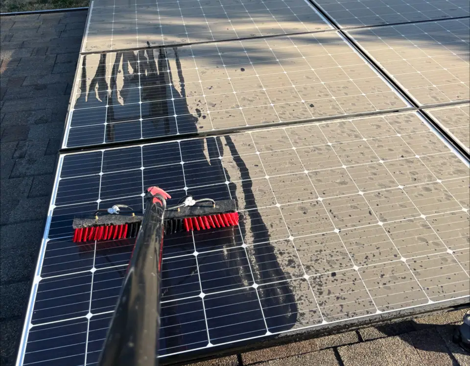 Red cleaning brush on solar panels with visible dusty and rinsed sections