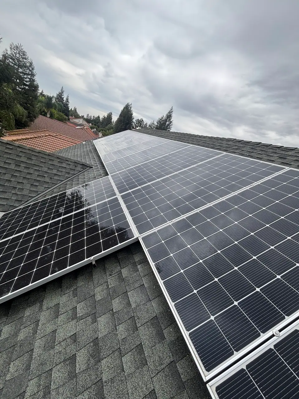 Solar panels across a gray shingle roof beneath cloudy skies