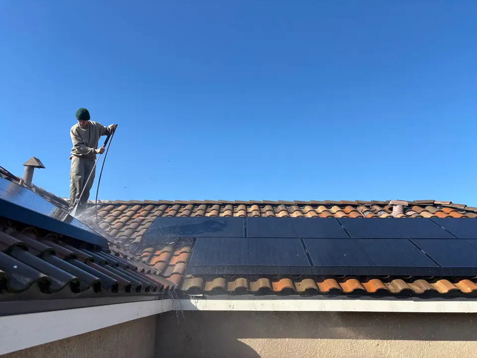 Technician holding a long cleaning pole beside solar panels on a tile roof