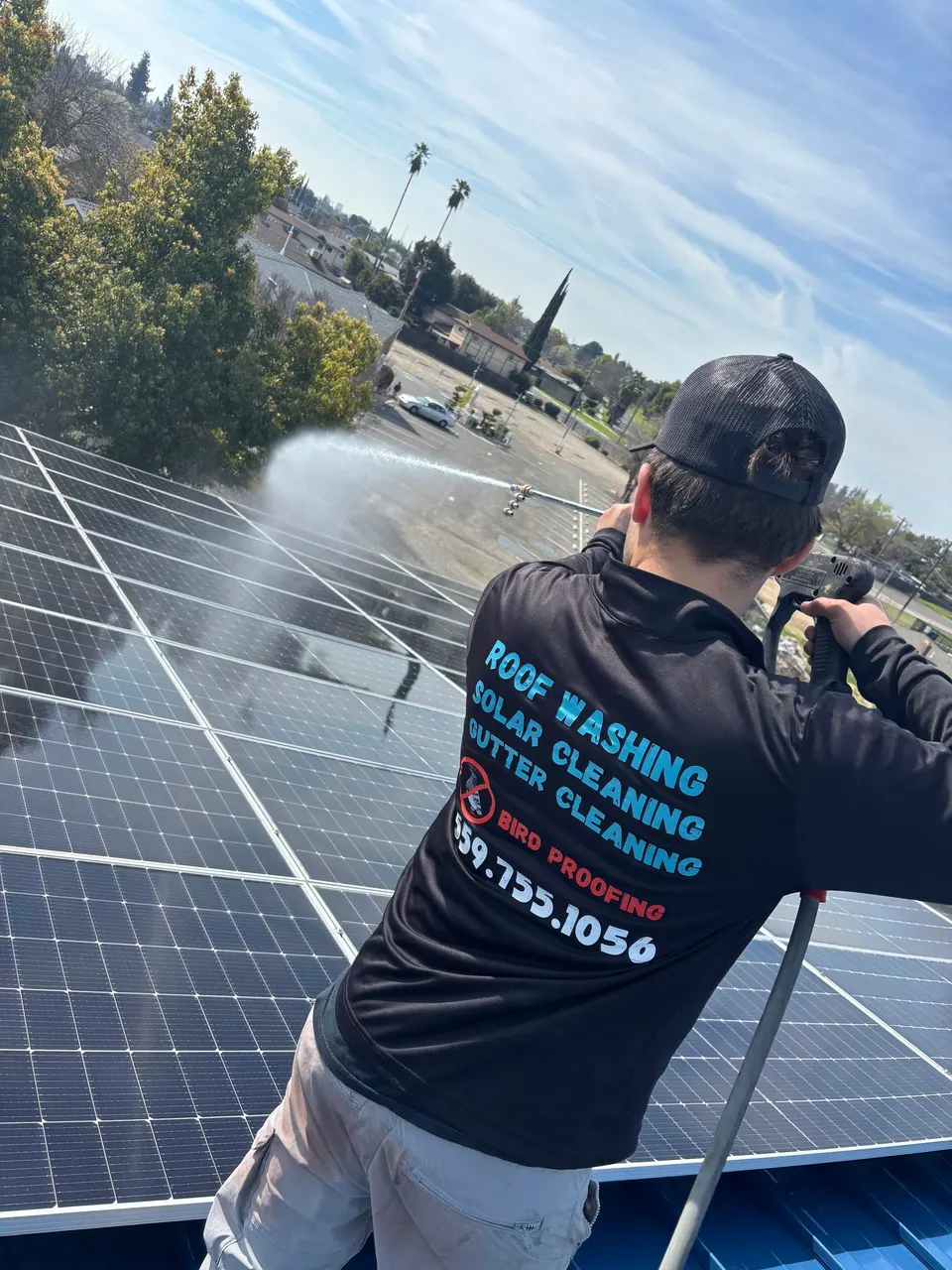 Technician wearing a CA Solar Wash shirt cleaning rooftop solar panels