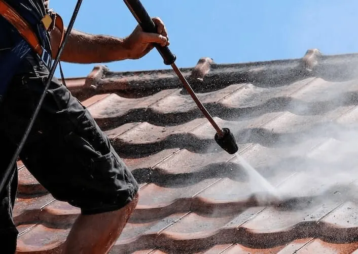 Spray wand washing dirt from a curved tile roof